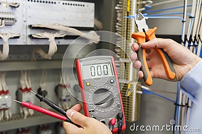 Tester and wire cutters in hands of electrician against electric control panel of automation equipment Stock Photo