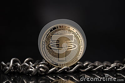 Tether USDT cryptocurrency physical coin placed next to metal chain on reflective surface in the black background Editorial Stock Photo