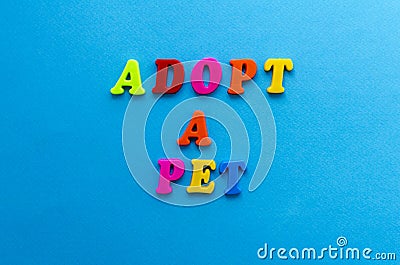 Text adopt a pet from plastic colored letters on blue paper background Stock Photo