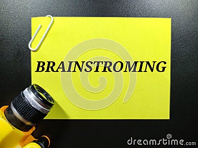 Text BRAINSTROMING on color paper with paper clips and keychain camera with blakc background. Stock Photo