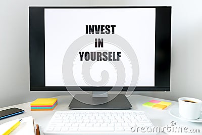 Text displayed on the monitor, Invest in Yourself. A desk with a keyboard, office accessories and a cup of coffee. The concept o Stock Photo