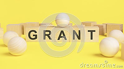 text GRANT on wooden cubes. bright yellow surface. wooden sphere balls among the wood cube Stock Photo