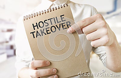 Text HOSTILE TAKEOVER on brown paper notepad in businessman hands in office. Business concept Stock Photo