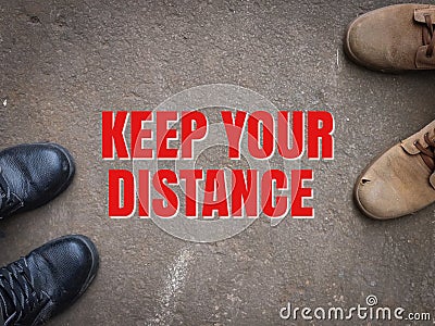 Text KEEP YOUR DISTANCE with safety shoes on asphalt road. Stock Photo
