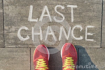 Text last chance written on gray sidewalk with women legs in sneakers, top view Stock Photo