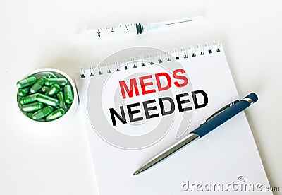 Text Meds Needed written in a notebook with a blue pen and a bunch of pills Stock Photo