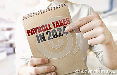 Text PAYROLL TAXES IN 2024 on brown paper notepad in businessman hands in office. Business concept Stock Photo