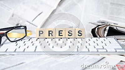 Text Press on wooden cube with a computer keyboard, newspapers and eyeglasses Stock Photo