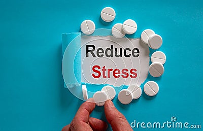 The text Reduce Stress appearing behind torn blue paper. White pills and male hand Stock Photo