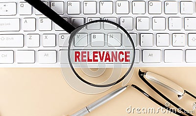 Text RELEVANCE on keyboard with magnifier , glasses and pen on beige background Stock Photo