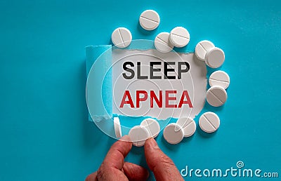 The text `sleep apnea` appearing behind torn blue paper. White pills and male hand Stock Photo