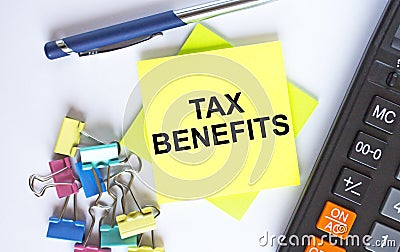 Text Tax Benefits on yellow stickers with calculator, blue pen and paper clips Stock Photo