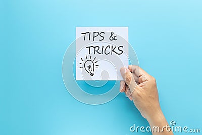 Text tips and tricks on white paper in hand isolated on blue background. Stock Photo