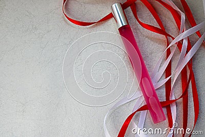 Texture with a pink matte thin long cylindrical perfume bottle, cologne with red and white beautiful festive ribbons made of artif Stock Photo