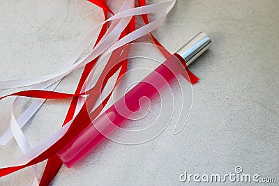 Texture with a pink matte thin long cylindrical perfume bottle, cologne with red and white beautiful festive ribbons made of artif Stock Photo