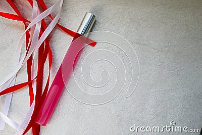 Texture with a pink matte thin long cylindrical perfume bottle, cologne with red and white beautiful festive ribbons made of artif Stock Photo