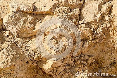 texture of a wall of sandy rock from a yellow friable old rotten stone of rock with shards, holes and layers of sand. The backgro Stock Photo