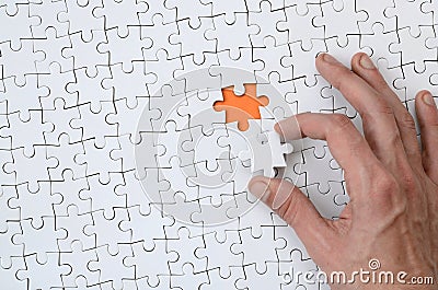 The texture of a white jigsaw puzzle in the assembled state with one missing element that the male hand puts in Stock Photo