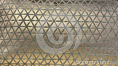 A textured fabric design featuring a repeating geometric triangular pattern in metallic gold and gray tones, creating an Stock Photo
