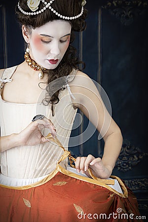 An 18th-Century woman getting dressed. She`s wearing stays and panniers with a skirt over the top. Stock Photo