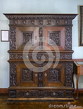 A 19th-century wooden carved cabinet made in Bavaria in the Old German Style, with a plaque on the wall describing its history Stock Photo