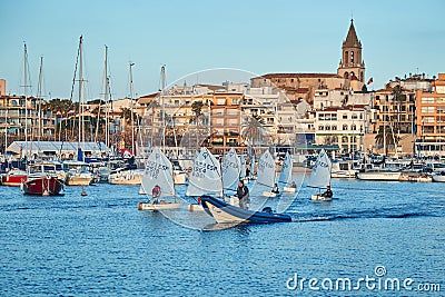 30th International Vila de PalamÃ³s Optimist Trophy, 14th Nations Cup. Sailboats sailing to the harbor small town Palamos in Editorial Stock Photo
