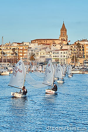 30th International Vila de PalamÃ³s Optimist Trophy, 14th Nations Cup. Sailboats sailing to the harbor small town Palamos in Editorial Stock Photo