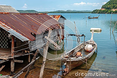 Thai fishing long boat next to the fisherman`s hut standing on stilts in the water. Editorial Stock Photo