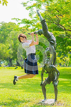 Thai schoolgirl is jumping with statue in park Stock Photo