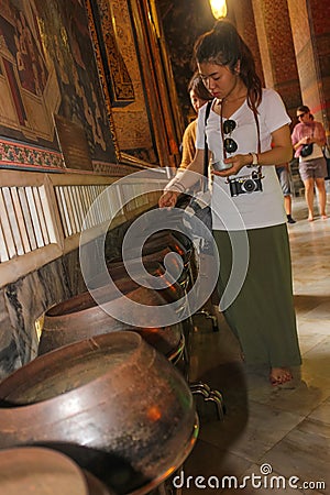 Bangkok, Thailand - April 29, 2014. Thai woman deposits coins as offering in a bowl of a monk at temple of the Reclining Golden Editorial Stock Photo