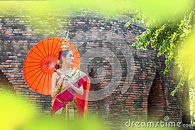 Thai Woman In Traditional Costume with umbrella of Thailand. Female Traditional Costume with thai style temple background. Wat Stock Photo