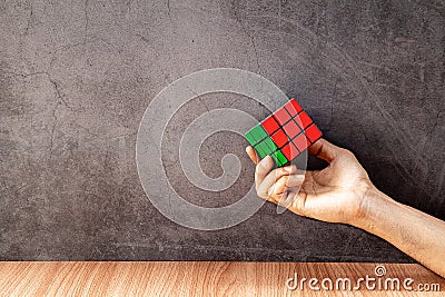 Thailand, bangkok. February 7, 2020. A man`s hand holding rubik`s cube on a wooden table with old gray concrete walls. Editorial Stock Photo