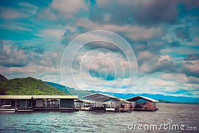 Thailand. Fisherman raft house in big lake with mountain and tree in the background in cloudy day , Floating houses in Kanchanabur Stock Photo