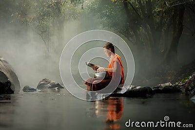 Thailand Little monk sitting on the creek or river in forest at Stock Photo