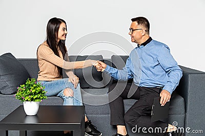 Thank you doctor. Cheerful male psychiatrist shaking hand to beautiful young woman sitting close to him Stock Photo