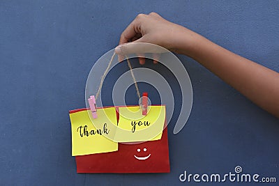 Thank you vintage style word on colorful origami paper notes. Young girl holding thank you sign rope with smiling emoticon on blue Stock Photo