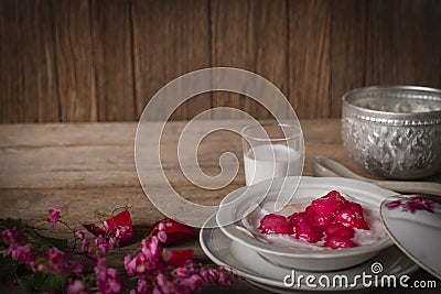 Thapthim krop, mock pomegranate seeds in coconut and syrup in the white bowl on the wood table there are flower, spoon, coconut Stock Photo