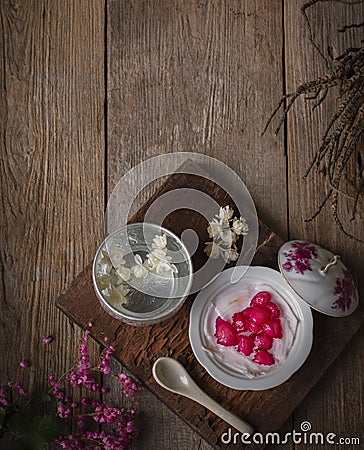 Thapthim krop, mock pomegranate seeds in coconut and syrup in the white bowl on the wood table there are spoon, flower and water Stock Photo