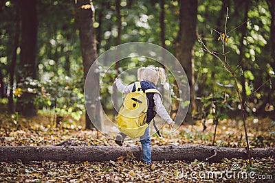 The theme children outdoor activities. Funny little baby Caucasian blond girl walks through forest overcoming obstacles, tree fell Stock Photo
