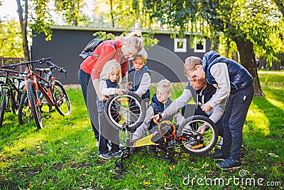 The theme is teamwork and a close-knit family spirit. Solving problems together. Big friendly family repairing a bike in the park Stock Photo