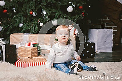 Theme winter and Christmas holidays. Child boy Caucasian blond 1 year old sitting home floor near Christmas tree with New Year dec Stock Photo