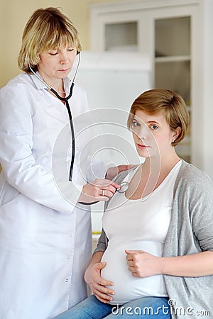 Therapist listens to a pregnant woman with a stethoscope. Medical insurance childbearing. Family doctor for gestation. Maternity Stock Photo