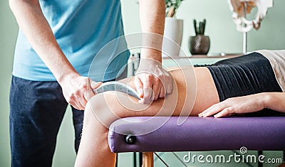 Therapist using IASTM instrument for soft tissue treatment on the leg of a female patient Stock Photo