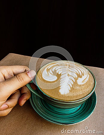 There is a cup of cappuccino on Kraft paper and it is held by a man`s hand, at the top of the frame there is plenty of space Stock Photo