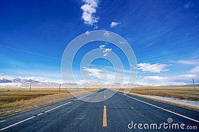 Endless straight road to snow mountains on plain with blue sky and white clouds Stock Photo