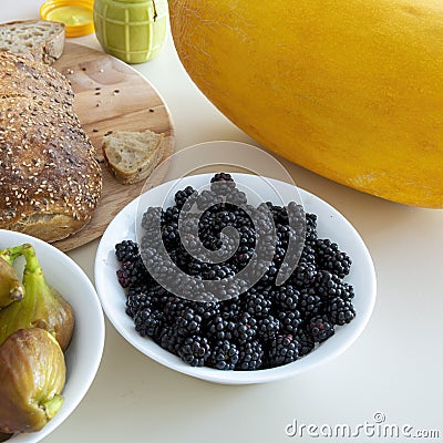 there are figs, bread and blackberries on the table, as well as a jar of honey with ginger and a large ripe melon Stock Photo