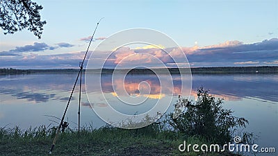 There is a fishing spot on the grassy shore of the lake. A feeder rod with an inertia-free reel is mounted on a fishing stand. Aft Stock Photo