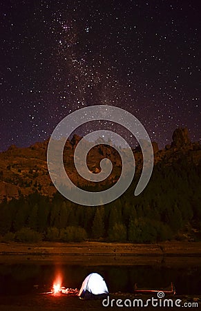 There is an illuminated tent near a river and a canoe on a starry night Stock Photo