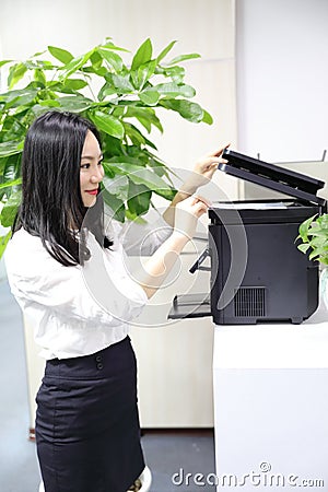 Asia Chinese office lady woman girl printing material use printer at work smile wear business occupation suit workplace Stock Photo