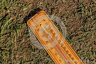 Thermometer displaying high summer temperature on a dry grass backgrou Stock Photo